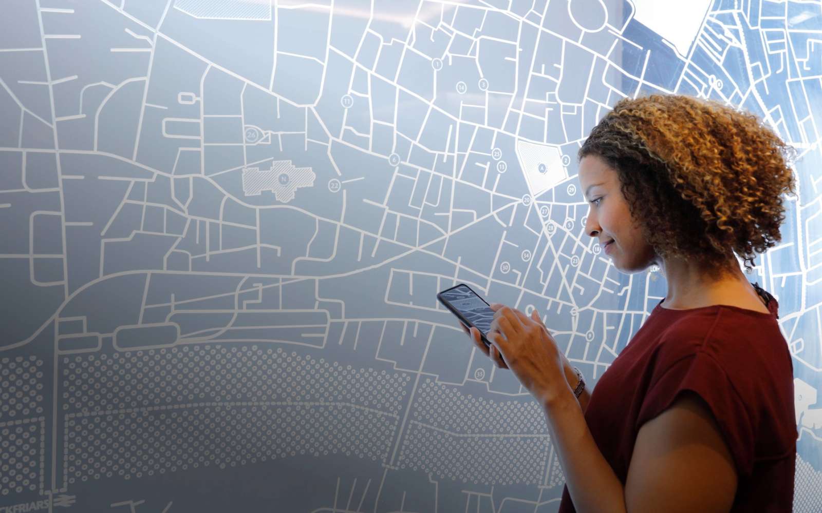 Person consulting a phone in front of a large wall-mounted city map of Ghent