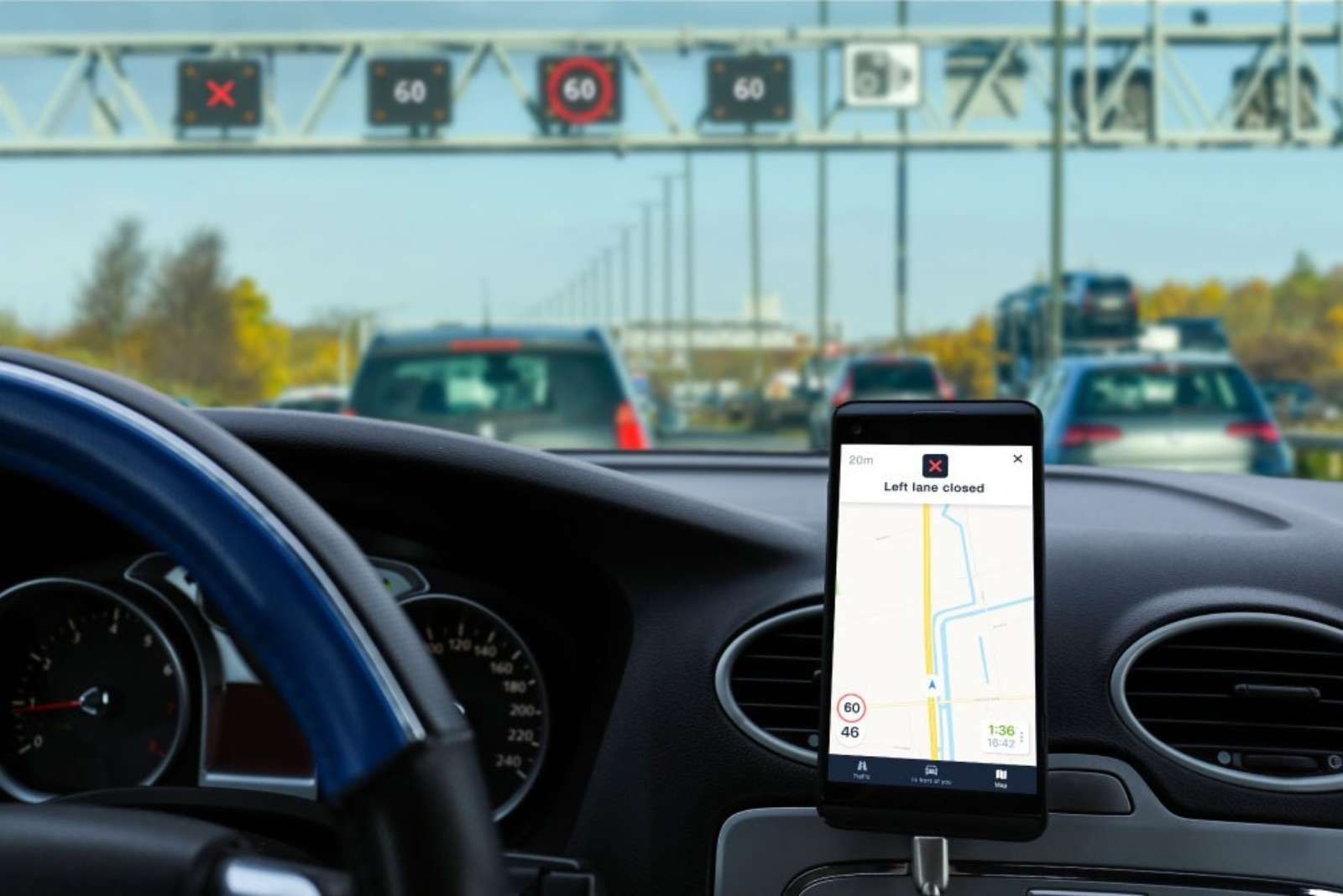 Driver viewing an in-car lane-closure warning while approaching motorway traffic-control signs.