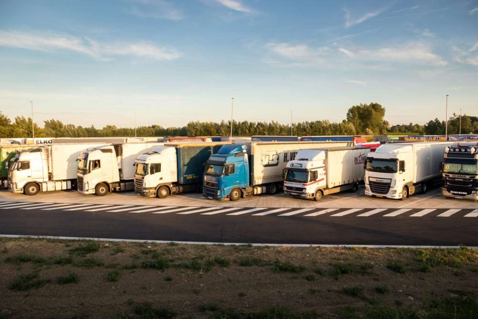 Row of semi-trucks parked at a freeway rest area at sunset