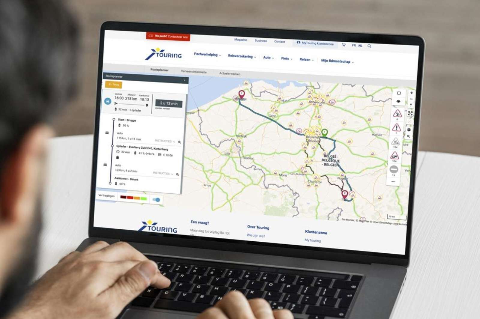 Person using a laptop showing the Touring route planner with a map of Belgium and a planned route with a charging stop