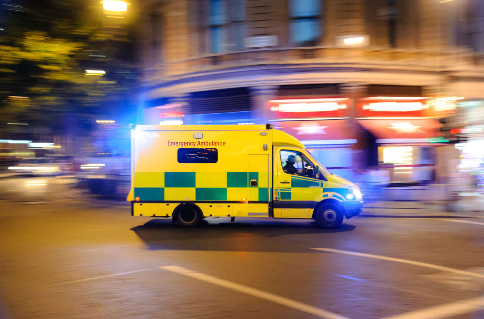 Emergency ambulance driving through a city street at night with blue lights flashing