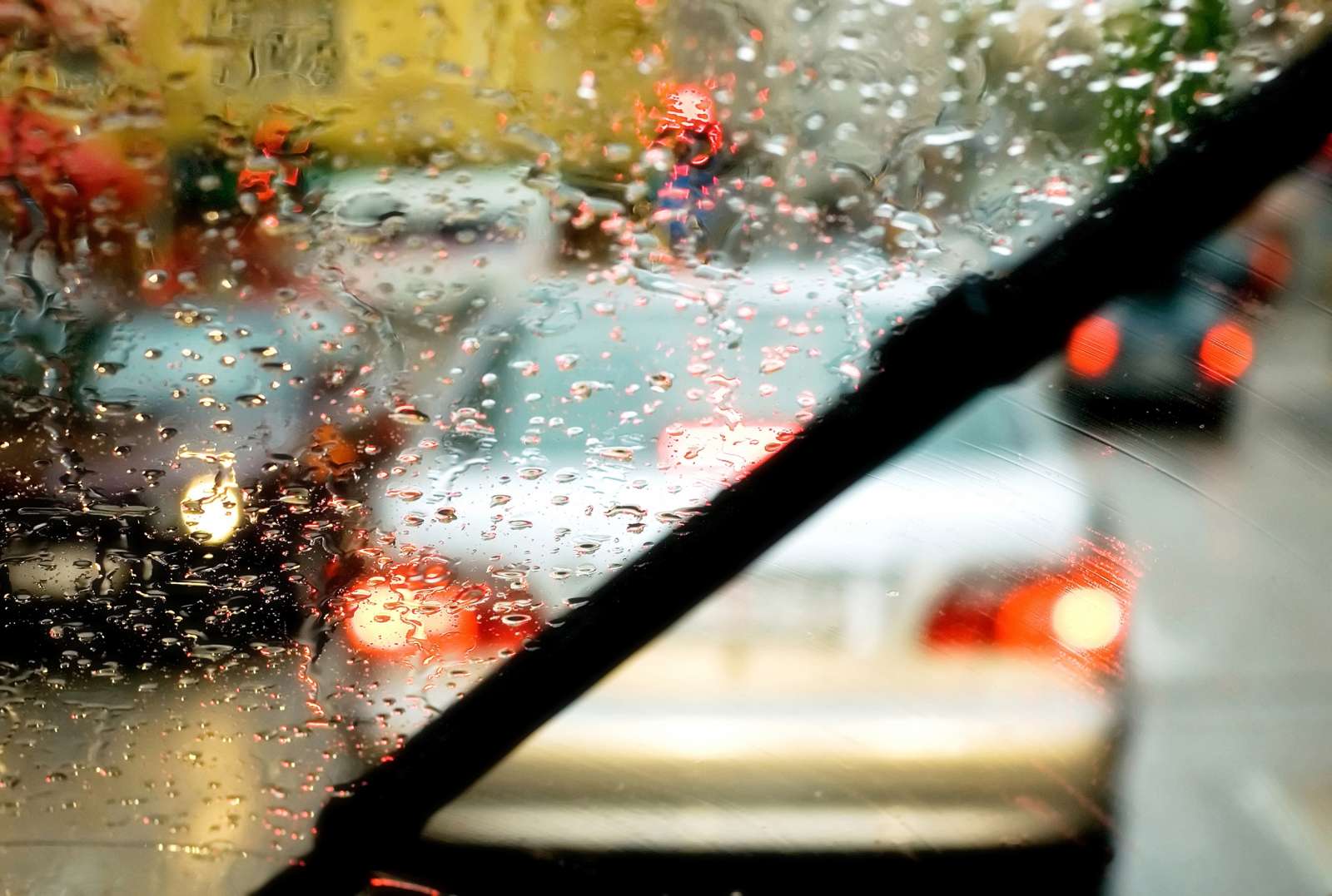 View through a rainy car windshield with wipers active, showing blurred tail lights in a traffic jam