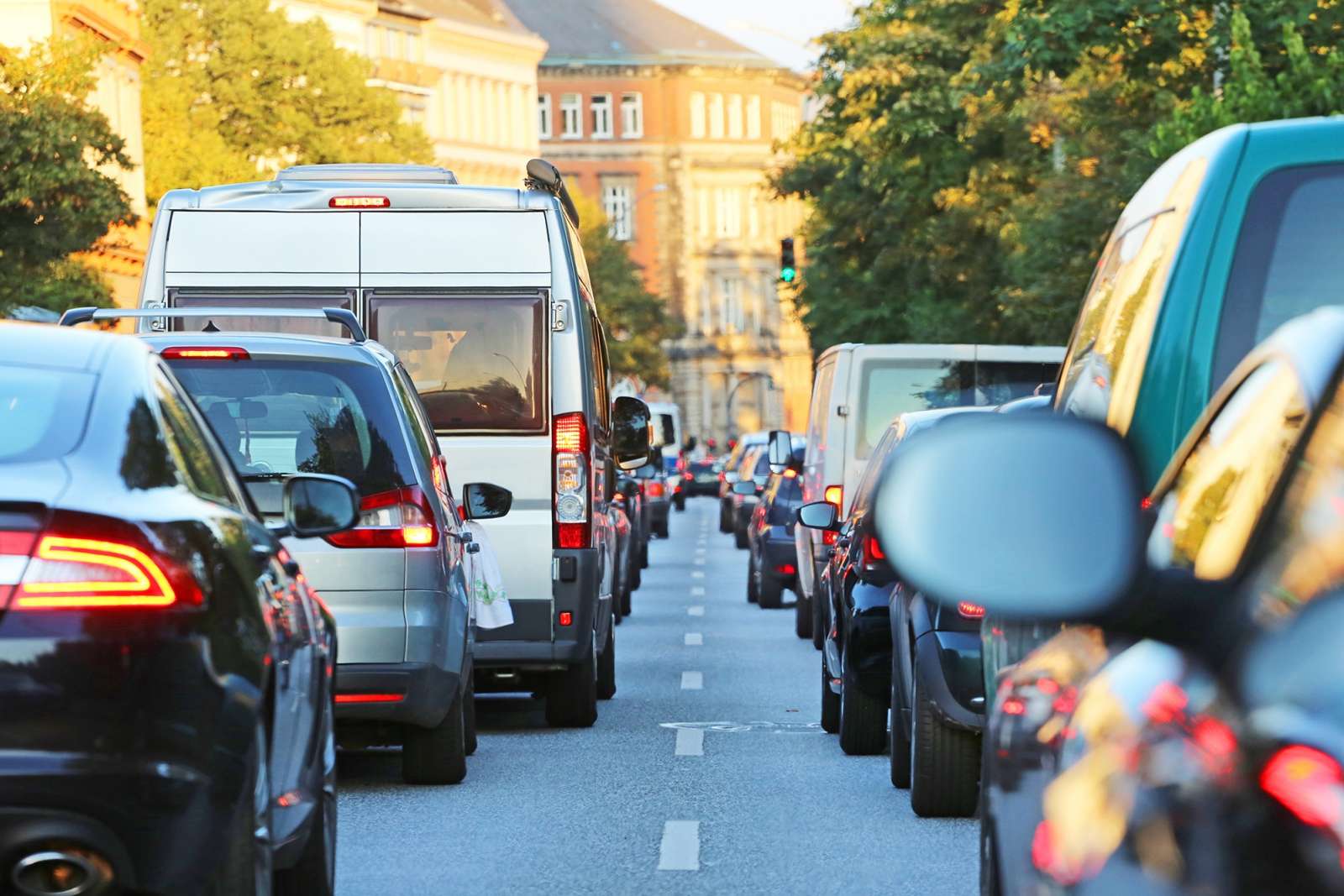Two queues of cars standing bumper to bumper in a city street lined with buildings and trees.