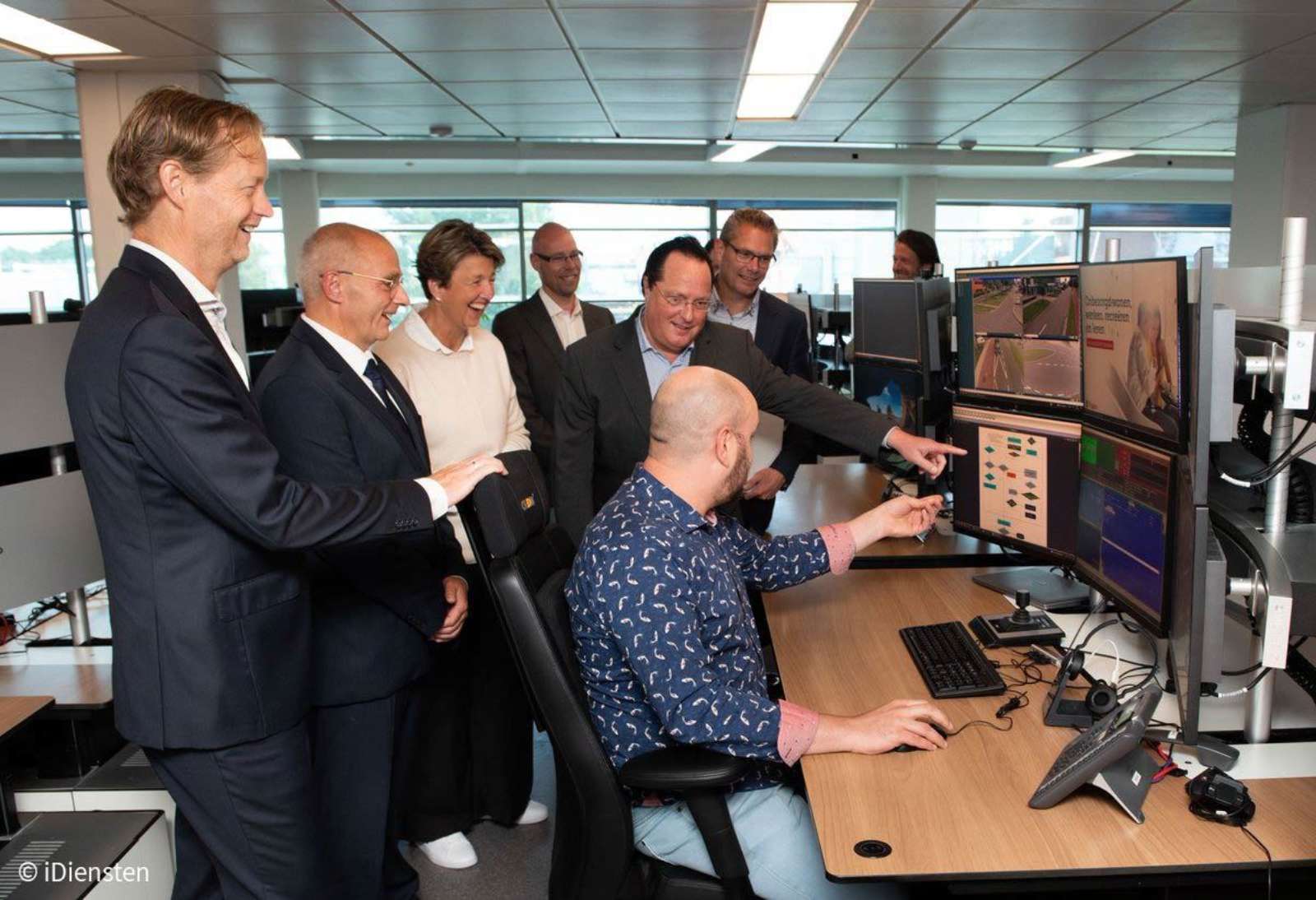 Officials gathered around a traffic control room workstation looking at monitors showing road camera views