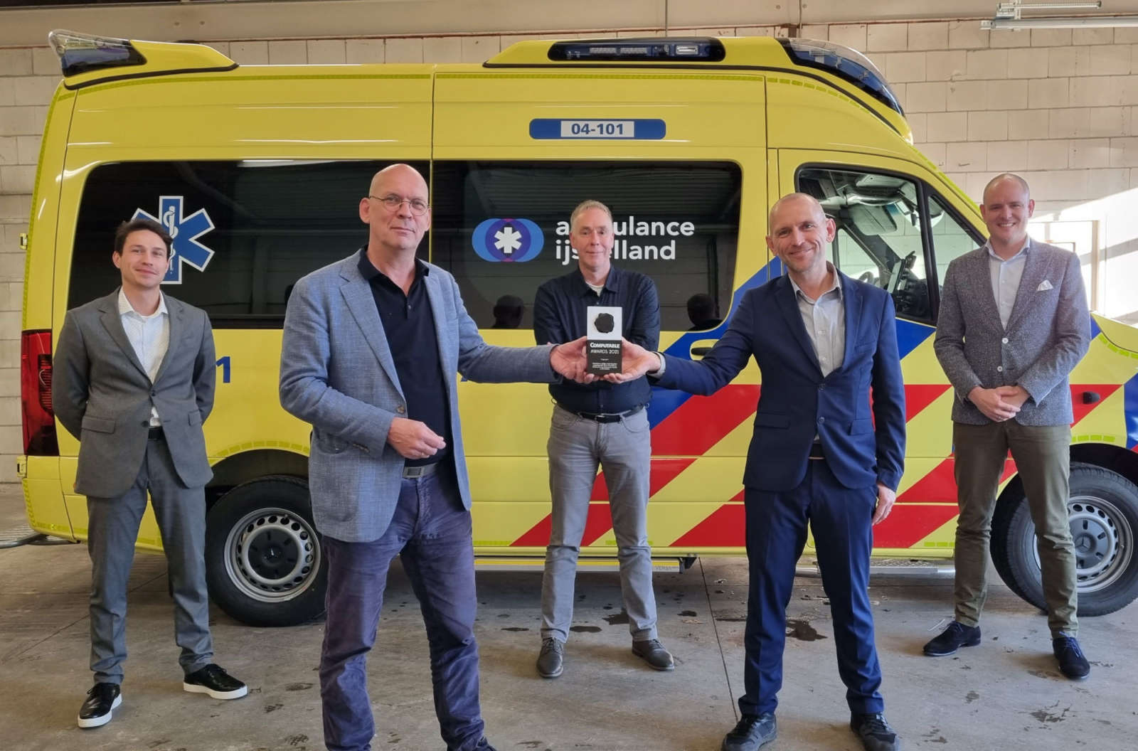 Five men standing in front of a yellow Ambulance IJsselland vehicle, two of them holding the Computable Awards 2021 trophy between them.