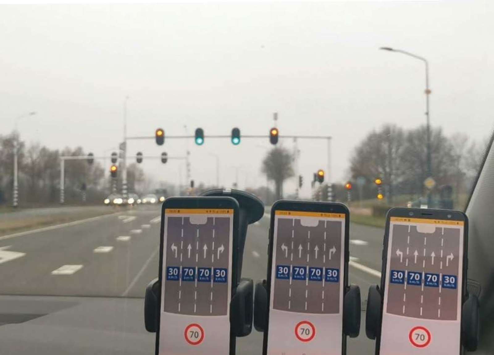 Three smartphones on a car dashboard showing lane-level GLOSA speed advice approaching a Dutch intersection